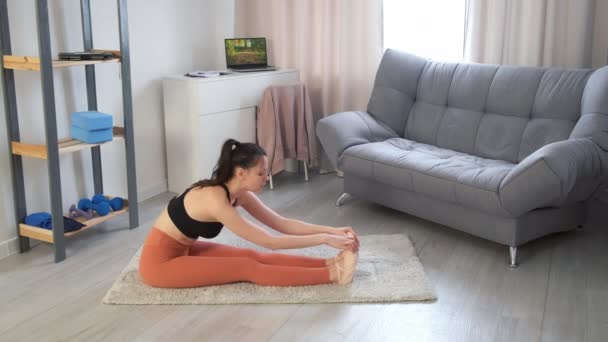 Jonge vrouw is het beoefenen van yoga doen zittend voorwaarts buigen houding op tapijt thuis. — Stockvideo