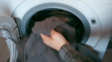 Çamaşır makinesini yatak örtüsüyle dolduran, evde çamaşır yıkayan insanlar..