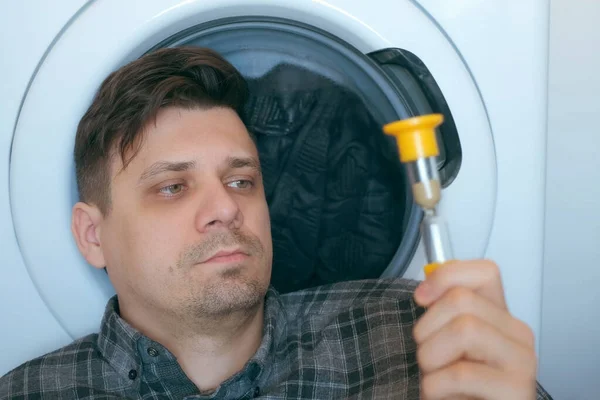 Mann mit Sandglas wartet auf Waschmaschine mit grauer Bettdecke darin. — Stockfoto