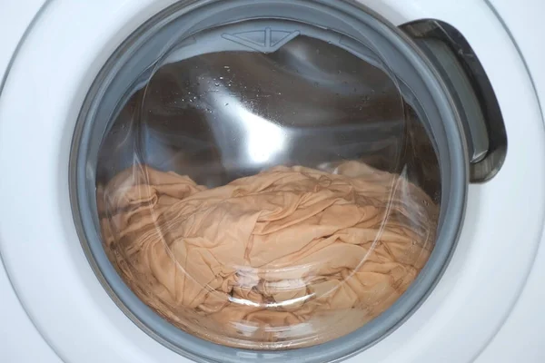 Washing machine wrings out the laundry beige bed linen, closeup window view. — Stock Photo, Image