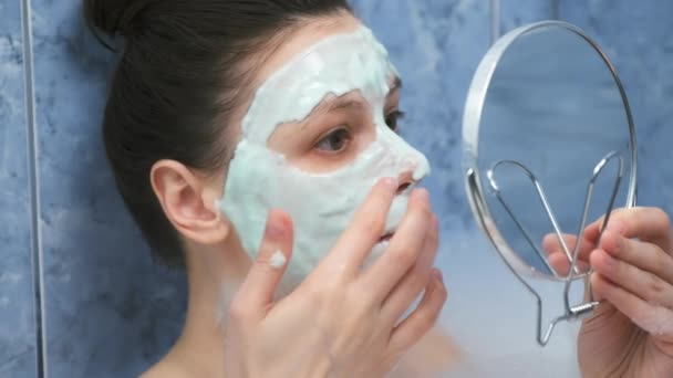 Kobieta nakłada alginianową maskę w wannie z pianką patrząc na małe lusterko. — Wideo stockowe