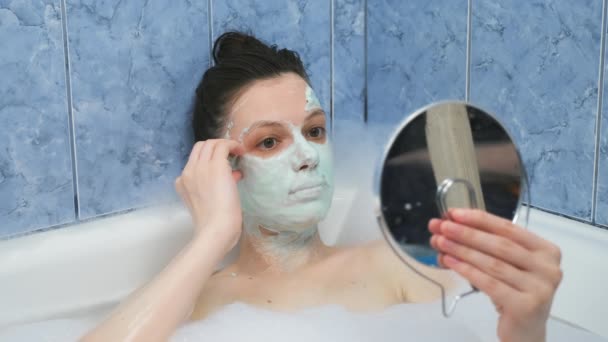 Jeune femme enlève masque en alginate de son visage couché dans la salle de bain avec de la mousse. — Video