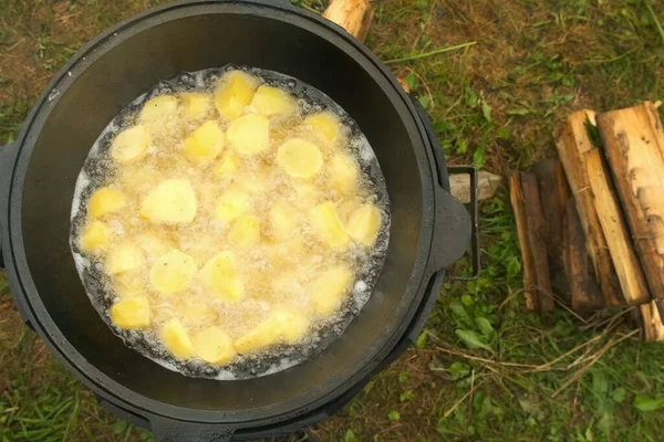 Potato is frying in cauldron in oil on nature on fire, closeup top view. — Stock Photo, Image