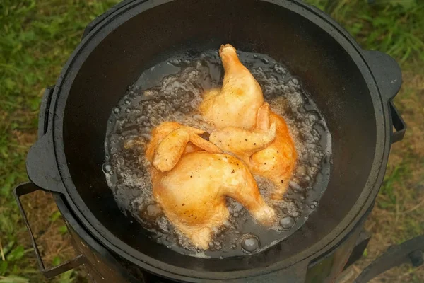 Frying chicken in black cazan with boiling oil in wood-burning stove on nature. — Stock Photo, Image