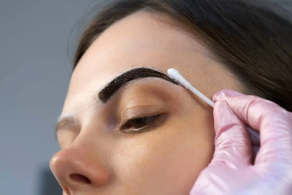 Cosmetologist is painting womans eyebrows in cosmetology clinic, closeup view.