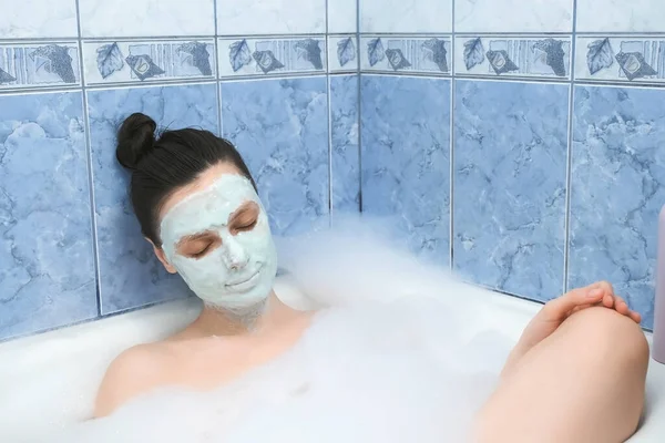 Молодая женщина с альгинатной маской расслабляется лежа в ванной комнате с пеной дома. — стоковое фото
