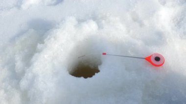 Kış balıkçılığı sırasında buzda balık tutma deliğinin yanında kırmızı balıkçı oltası sallanıyor. Açık hava kış aktiviteleri hobi eğlence sporu gibi bir şey. Balık yakalama yarışması.
