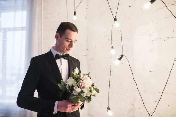 Handsome young groom in a tuxedo with a butterfly is holding a w — Stock Photo, Image