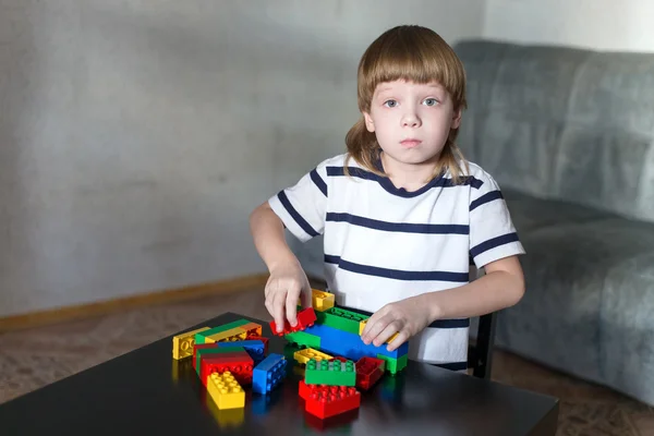 Мальчик играет с большим количеством красочных пластиковых блоков в помещении — стоковое фото