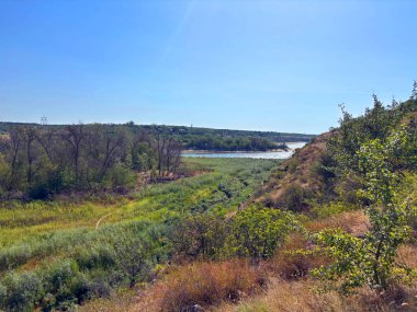 Parlak yaz güneşinin ışığında, saydam bir bozkır nehrinin manzarası aşırı gelişmiş çayırların ve taş bariyerlerin arasından geçiyor..