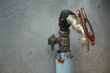 Paslı ve eskimiş desenli eski metal musluk beton bir duvara karşı antika bir cazibe, endüstriyel estetik ve zamanın geçişini çağrıştırıyor..