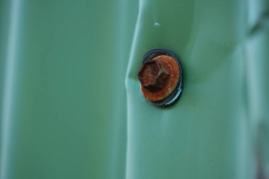 Yeşil metal bir yüzey üzerinde paslı bir vidanın yakın plan görüntüsü, endüstriyel detaylar ve dokular sergiliyor, vidanın paslanmış durumuna ve etrafındaki metallere odaklanıyor..