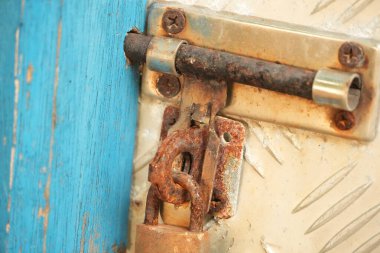 Paslı bir kapı mandalının yakın çekim görüntüsü ve yıpranmış mavi ve metal bir kapı yüzeyi, yaşlanma ve çürüme belirtileri gösteriyor..