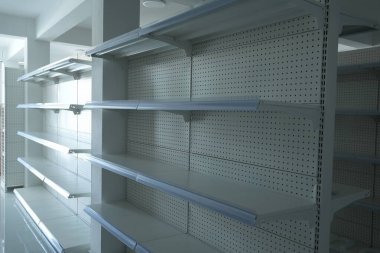Beyaz tahta destekli bir sıra boş raflar ve metal raf üniteleri, temiz ve minimalist estetik bir perakende alanındaki doğal ışıkla aydınlatılıyor..