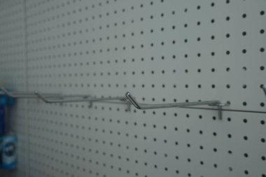 Eşit aralıklı delikleri ve metal kancaları olan gri bir tahta atölye veya garajda alet ve teçhizat düzenlemek, verimliliği ve erişilebilirliği teşvik etmek için.