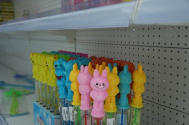 Bir mağaza rafında, tavşanlara ve canavarlara benzeyen, berrak tüpler ve parlak kapaklı, çocuklara hitap eden çeşitli renkli baloncuk kalemler sergileniyor..