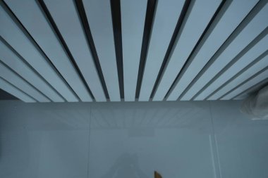 Beyaz panelleri ve havalandırma sistemi olan modern, yumuşak bir tavana yakından bakmak çağdaş uzayda gösterişli ve minimalist bir tasarım sergilemektedir..