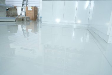 Pürüzsüz, modern bir iç mekan. Beyaz duvarlar ve dolaplar eşliğinde arka planda merdiven ve kutular bulunan parlak bir kaplaması var..