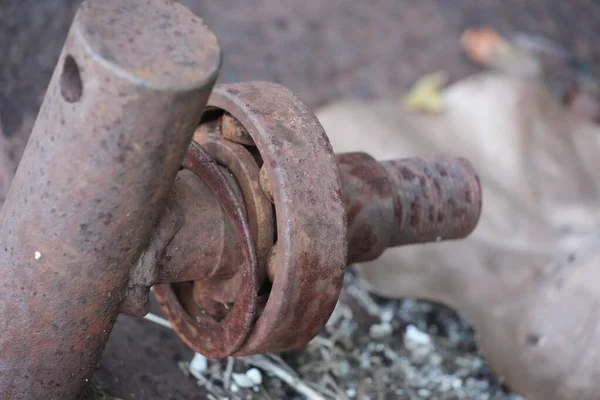 Paslı bir metal eklem ya da menteşenin yakından görüntüsü, paslanma ve kir ile kaplı, yaprakların ve molozların arasında yerde yatıyor, çürümeyi ve ihmalkarlığı gösteriyor..
