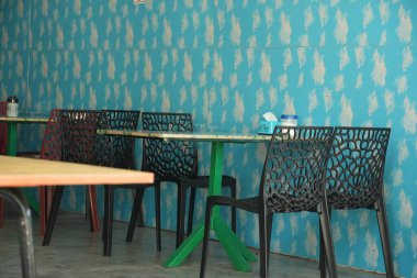 Beyaz desenli mavi bir duvar, yeşil masa tabanı ve eşsiz tasarımları olan siyah sandalyeler içeren canlı bir restoran iç mimarisi, canlı bir atmosfer yaratıyor..