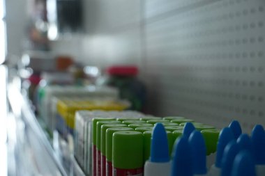 A long line of glue bottles with brightly colored caps, predominantly green and blue, is neatly arranged on a shelf in a retail setting.
