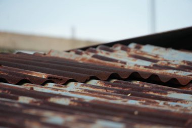 Bu görüntü, eski bir bükülmüş metal çatının zengin ve paslı dokusunu yakalar. Dalgalı paneller yoğun bir şekilde oksitlenmiş, sessiz gökyüzüne karşı sıcak kahverengiler ve portakallar sergiliyorlar..