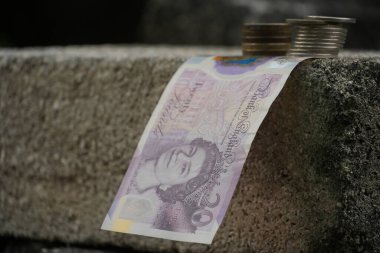 İngiliz 20 pound 'luk banknot, koyu, tanımlanmamış bir arka plana karşı, desenli beton bir kenar üzerinde zarif bir şekilde perdelenir..