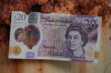 İngiltere 'de 20 poundluk banknot, zenginleştirilmiş, paslanmış metal bir yüzeyin arka planıyla keskin bir tezat oluşturarak, finans ve çürüme temaları vurguluyor..