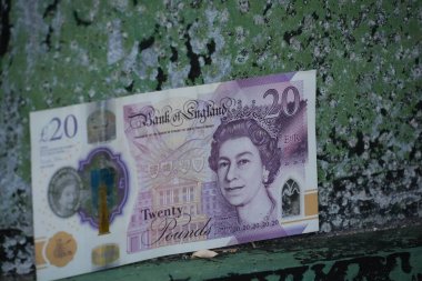 Bu resim, finans ve kentsel bozulma temaları için uygun, yeşil ve mavi kabuklu boyanın sıkıntılı arka planına karşı 20 pound değerinde bir banknot içeriyor..