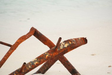 Ağır paslanmış metal parçaları, muhtemelen eski borular ya da bir yapının parçası, kısmen bir kumsalın el değmemiş beyaz kumuna gömülüp, insan doğası üzerindeki etkisini ima ediyor..