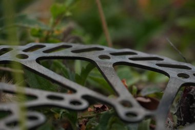 Metalik dokusunu ve mekanik tasarımını sergileyen bir bisiklet disk fren pervanesinin ayrıntılı bir çekimi, yeşil açık hava yeşillikleri ve zemin arasında yer almaktadır..