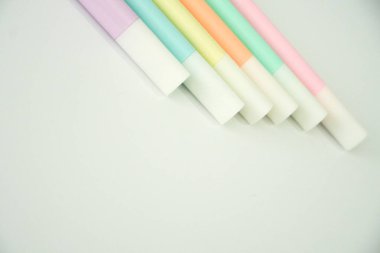 Pastel fosforlu kalemler derlemesi parlak, düzensiz beyaz zemin üzerinde yaratıcılığı ve eğitimi sembolize eden nazik çapraz bir çizgi oluşturur..