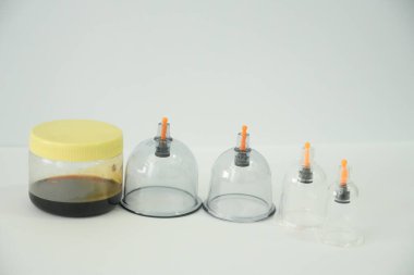 Dört şeffaf bardak, geleneksel sağlık uygulamaları ve çareleri vurgulayan, muhtemelen bitkisel, sıvı bir kavanoz ile sergileniyor..