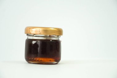 Büyüleyici küçük cam bir kavanoz, altın kapakla sıkıca kapatılmış, el değmemiş beyaz arka planda zengin, siyah bal sergileniyor..