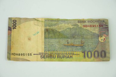 Bu resim, dağları ve su kütlesi olan sakin bir ada manzarasının yer aldığı eski bir Endonezya Rupiah notasının arkasını çekiyor..