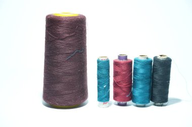 Bu resim, büyük bir koyu iplik maketi ile dört küçük, enerjik makara arasındaki kontrastı vurgular, el işi veya tekstil temaları için idealdir.