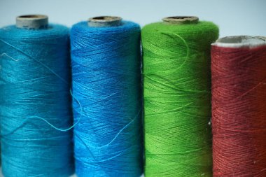 Mavi, yeşil ve kırmızı iplik makaralarının detaylı görünümü, dokularını ve canlı renklerini vurguluyor.