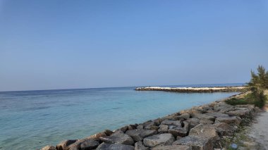 El değmemiş turkuaz okyanus dalgaları engebeli, doğal kayalık bir kıyı şeridine nazikçe sarılır güzel, geniş mavi bir gökyüzünün altında.