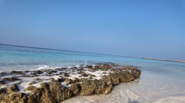 Sakin, berrak mavi okyanus suyuyla kayalık bir kıyı şeridi. Sakin bir gökyüzünün altında yavaşça kayalara çarpıyor..