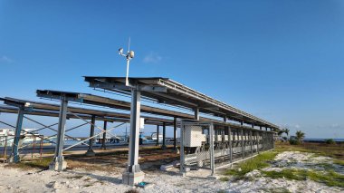 Etkileyici bir dizi güneş paneli, yenilenebilir enerjinin bir örneği, açık mavi gökyüzünün altında okyanus ve arka planda daha yeşil bir geleceği sembolize eden uzak tekneler ile duruyor..