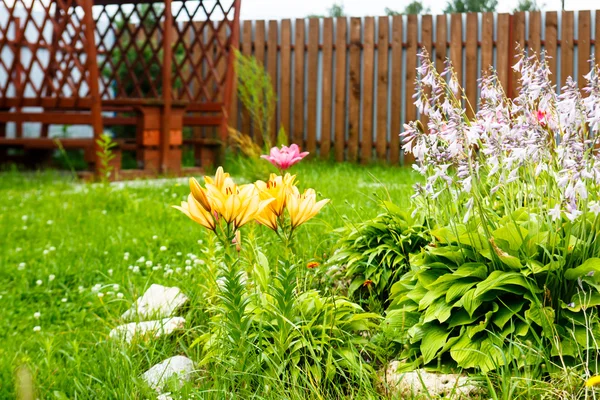 Lirios amarillos y campanas en un jardín con un gazebo en medio de gra verde — Foto de Stock