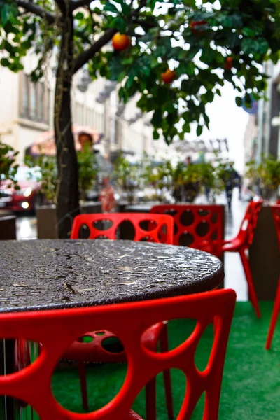 Café de rua na chuva, gotas de chuva na mesa preta e cadeira vermelha . — Fotografia de Stock