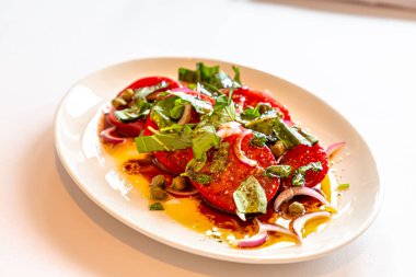 Tabakta soğan ve kapari ile taze domates salatası var..