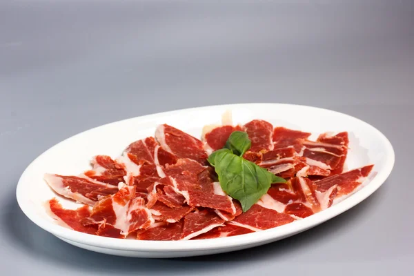 На тарелке нарезанная ветчина, прошутто, бекон, салями и другие мясные деликатесы . — стоковое фото