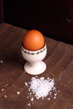 Karanlık tahtada kaba tuz ile yalan bir kahverengi yumurta.