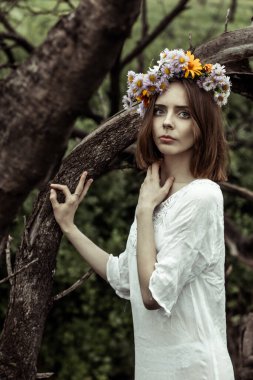 Çelenk takmış bir kız ağacın yanında duruyor.