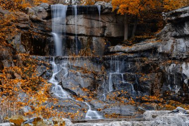 Sonbahar parkında altın çağlayan sular yavaşça karanlık kayaların üzerinden akar.