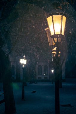 Sıcak sokak feneri, boş bir şehir parkında karlı karları aydınlatıyor.