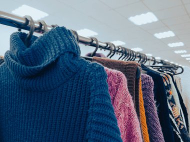 Parlak ışıkların altında askılarda sergilenen sıcak ve rahat süveterler.