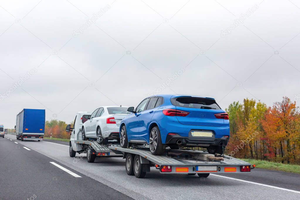 Truck transporter carrying new cars on the road. Colorful autumn trees background